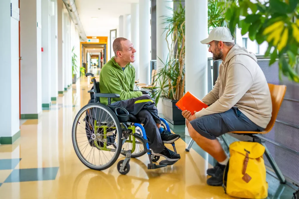 A disabled man sitting in his wheelchair and his support worker talking